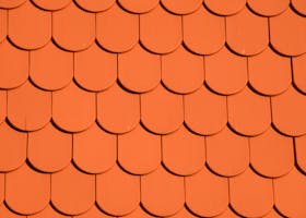 Bright orange roof tiles arranged in a seamless repetitive pattern, perfect for backgrounds and designs.